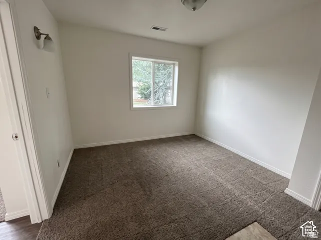 Room featuring neutral wall tones, window with white trim, wall-mounted light fixture, and textured carpeting