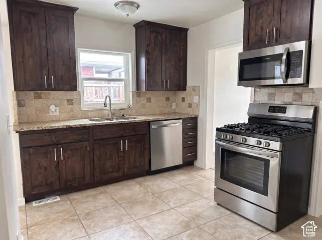 Kitchen featuring dark wood cabinetry, light-toned tiled flooring, a stainless steel gas range, a stainless steel microwave, and a stainless steel dishwasher