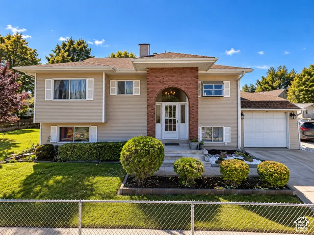 Split-level home featuring light-colored siding, an arched brick entry, an attached garage, and a concrete driveway
