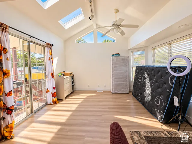 Vaulted ceiling with dual skylights, wood-finish flooring, ceiling fan, and sliding glass door