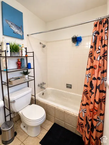 Bathtub with tiled surround, wall-mounted shower head, and tile flooring