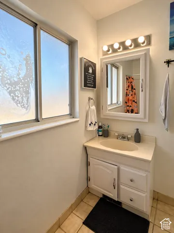 Single vanity with an integrated sink and base cabinetry, complemented by a wall-mounted mirror with an overhead light bar, and tile flooring