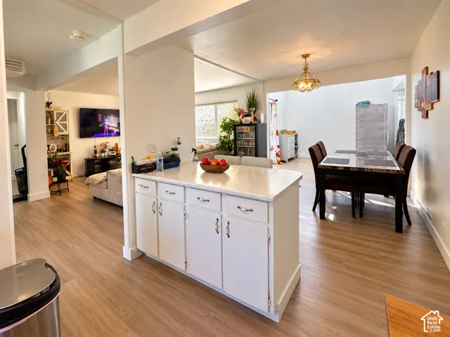 Central kitchen island with white cabinetry and a light-toned countertop, wood-finish flooring, recessed lighting, and an overhead dining room fixture