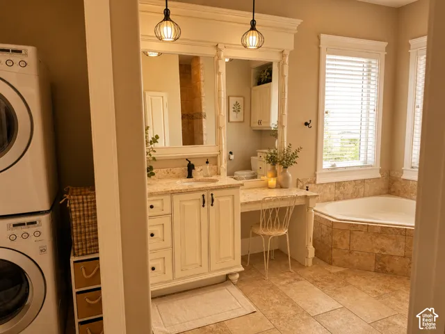 Built-in vanity with dual mirrors, corner soaking tub, stone tile flooring, and integrated laundry appliances