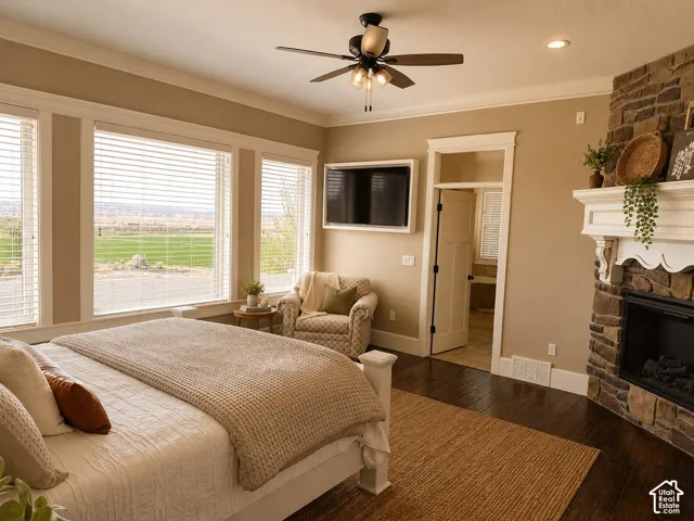 Stone-clad fireplace with mantel, dark wood-finish flooring, ceiling fan light fixture, multiple windows with horizontal blinds, and crown molding