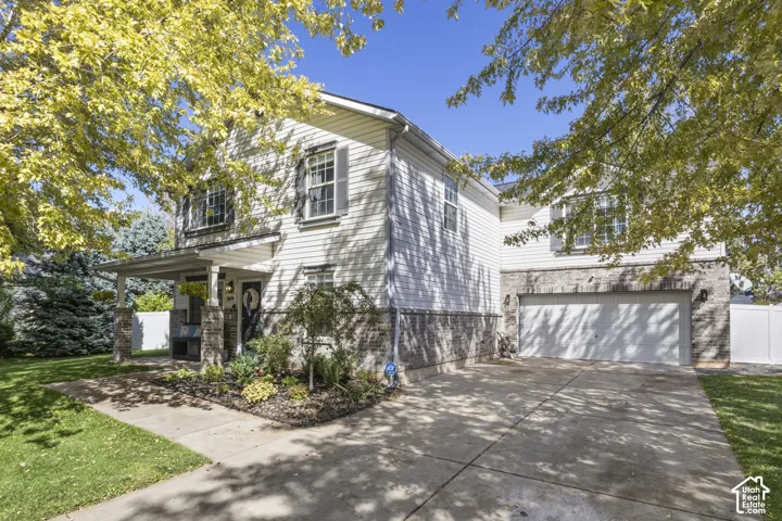 Two-story residence featuring white siding and a stone facade, a covered front porch, a two-car garage, and established landscaping