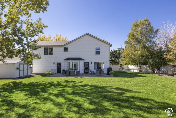 Expansive green lawn with mature trees, white siding exterior, and a large paved patio area