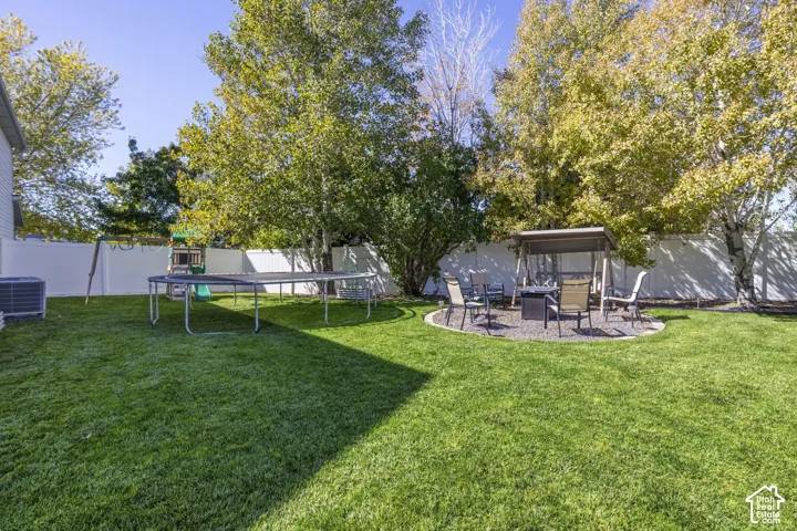 Expansive backyard featuring a manicured lawn, established perimeter trees, and a dedicated patio area with a gravel surface