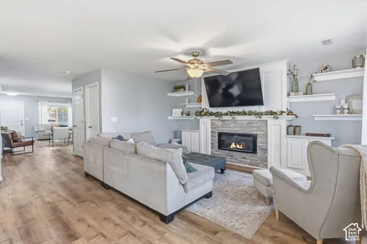 Living area featuring wood-finish flooring, a stone-faced fireplace with a white mantel, built-in shelving, and a ceiling fan