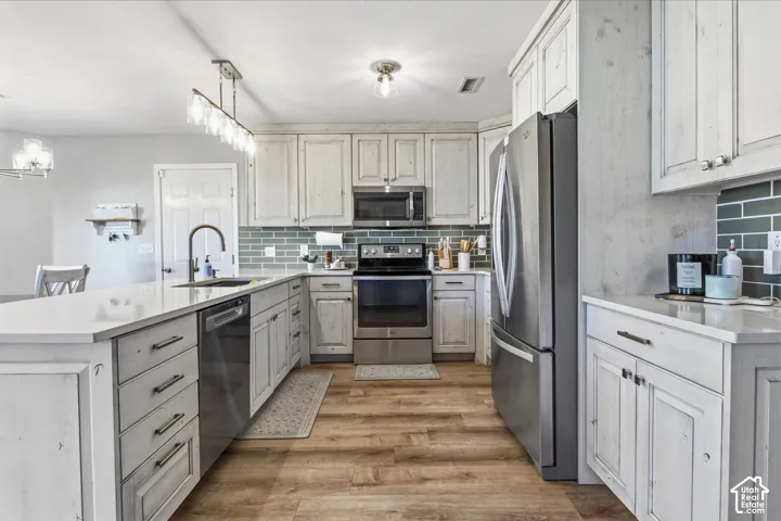 Kitchen featuring light-toned cabinetry, stainless steel appliances, a center island with sink, subway tile backsplash, and wood-finish flooring