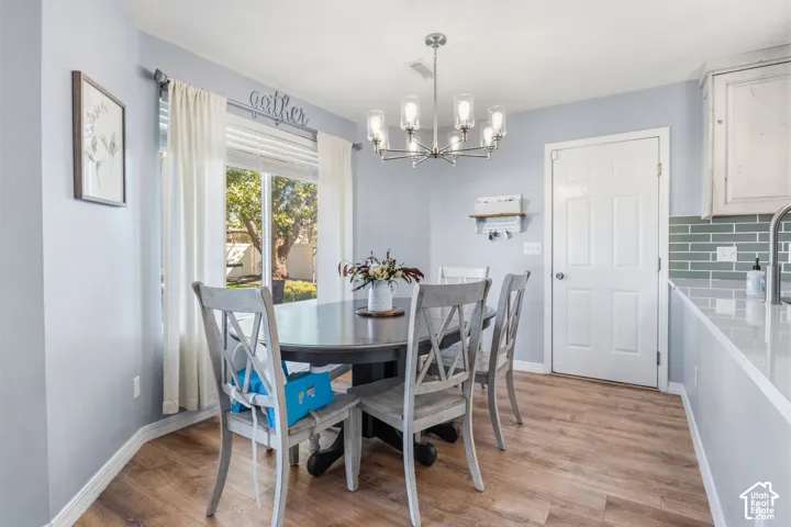 Dining area featuring wood-finish flooring, a large window, a modern chandelier, and a kitchen counter with a subway tile backsplash