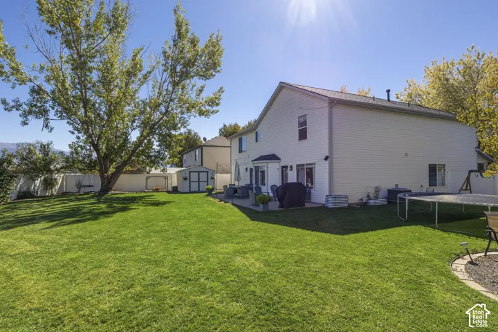 Expansive green lawn, mature trees, concrete patio, two-story exterior, and storage shed