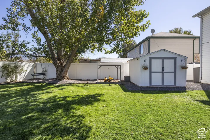 Expansive backyard featuring a manicured lawn, mature shade tree, and white privacy fencing