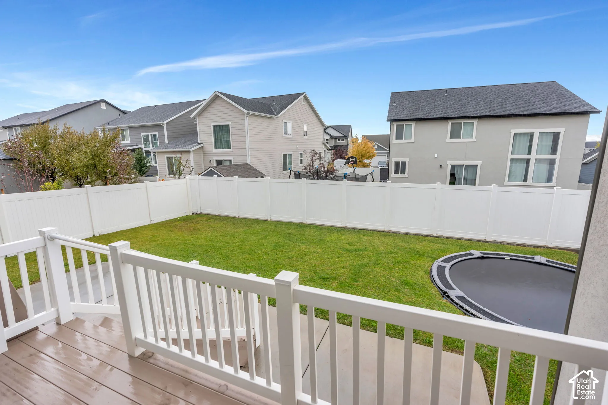 Expansive backyard oasis featuring a manicured lawn, white vinyl perimeter fencing, and composite decking with matching railings