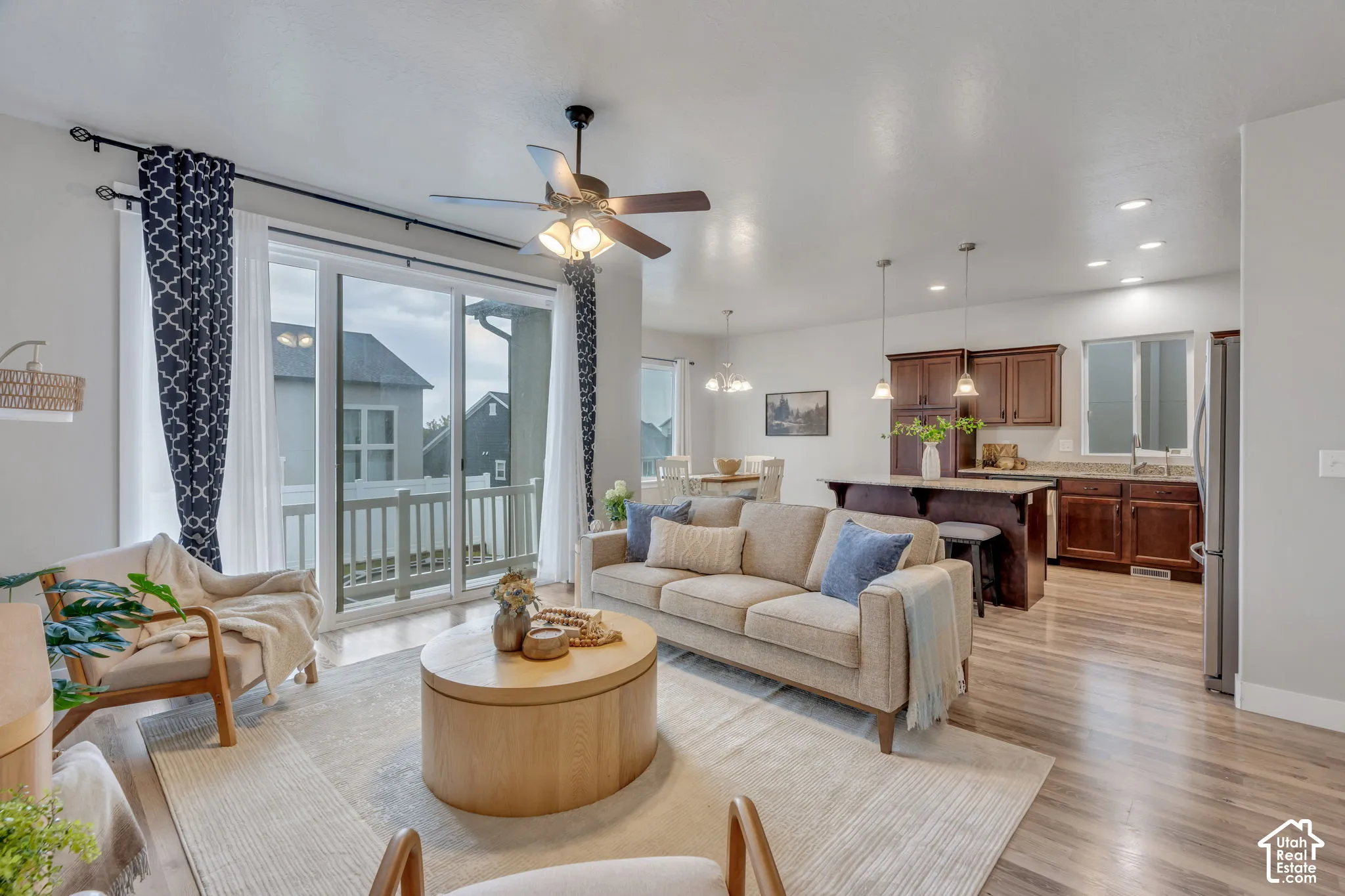Open-concept living space featuring hardwood flooring, a ceiling fan with integrated lighting, and expansive glass sliding doors opening to a covered exterior deck