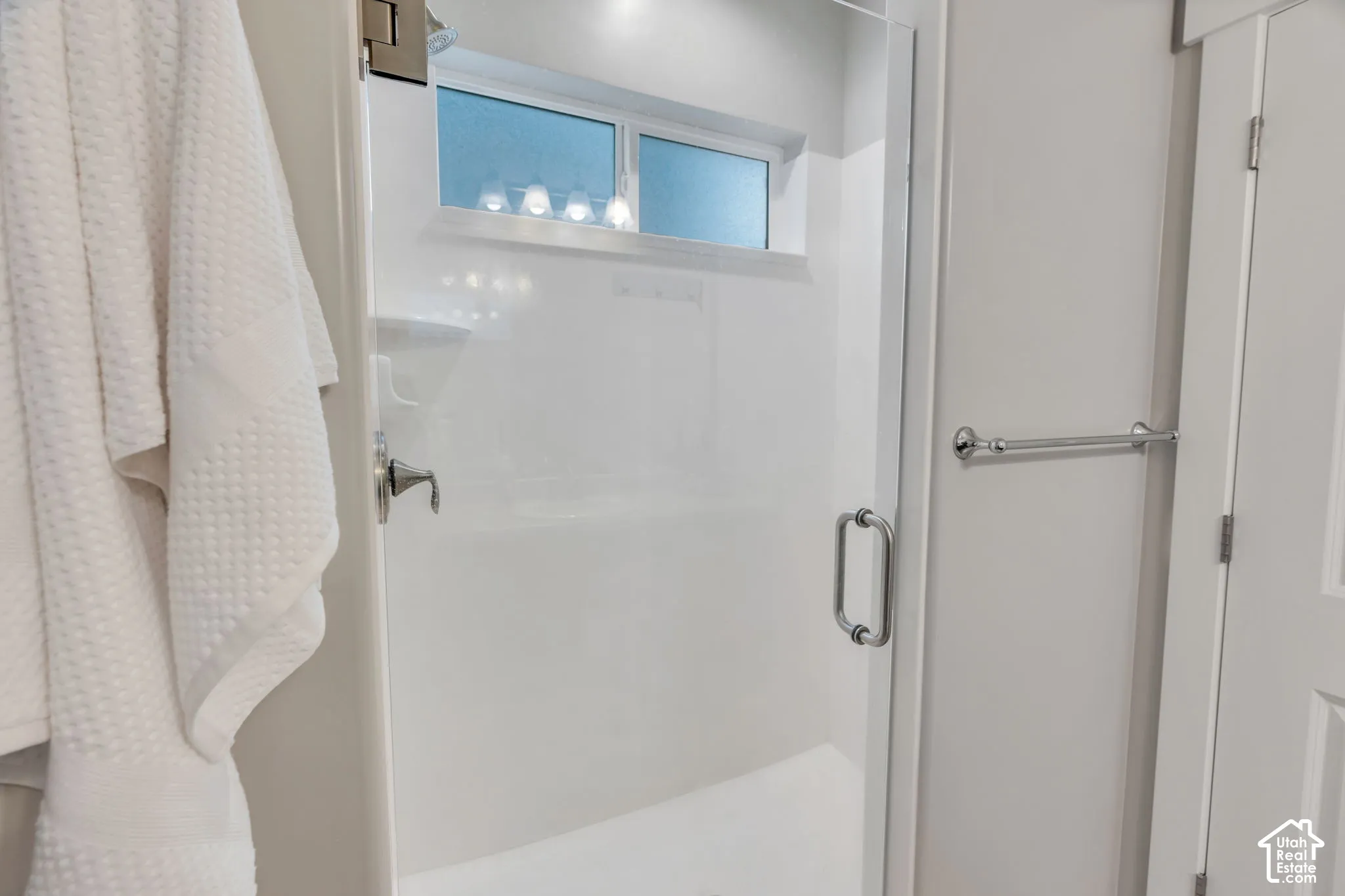 Glass-enclosed shower with a chrome handle, featuring a window and a wall-mounted shower fixture