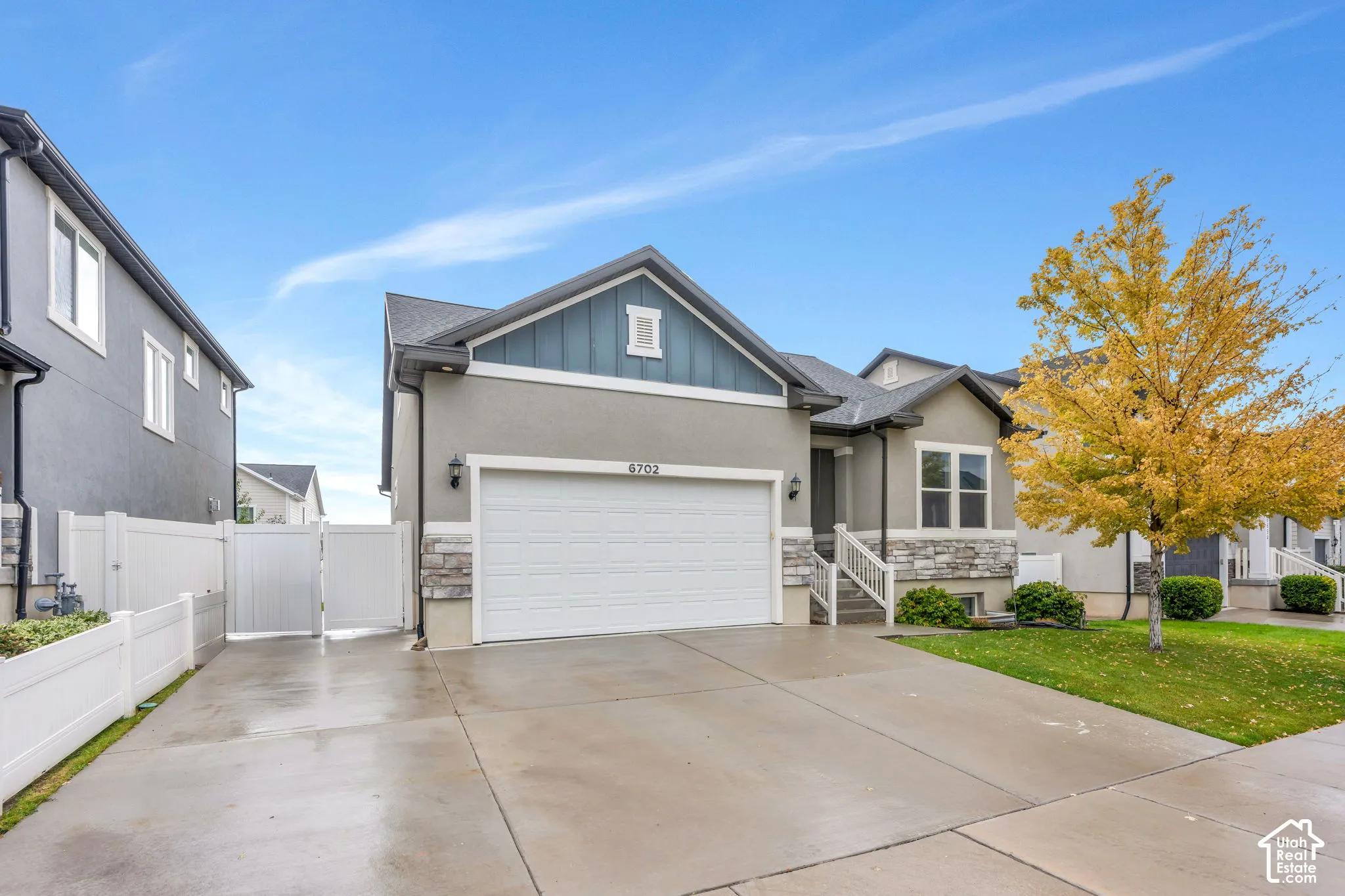Gray stucco exterior with stone accents, a two-car garage, a covered entry, and a white picket fence