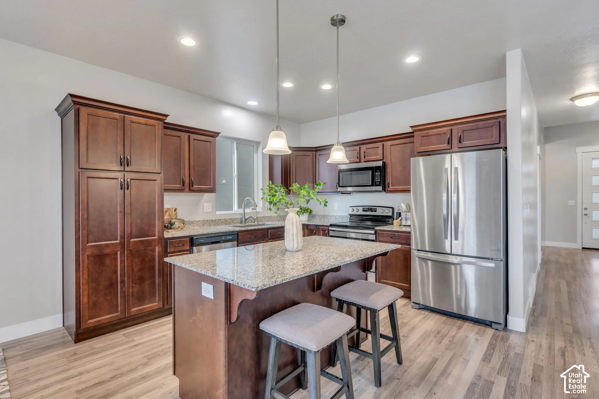 Kitchen featuring wood-finish flooring, dark wood cabinetry, granite countertops, and stainless steel appliances
