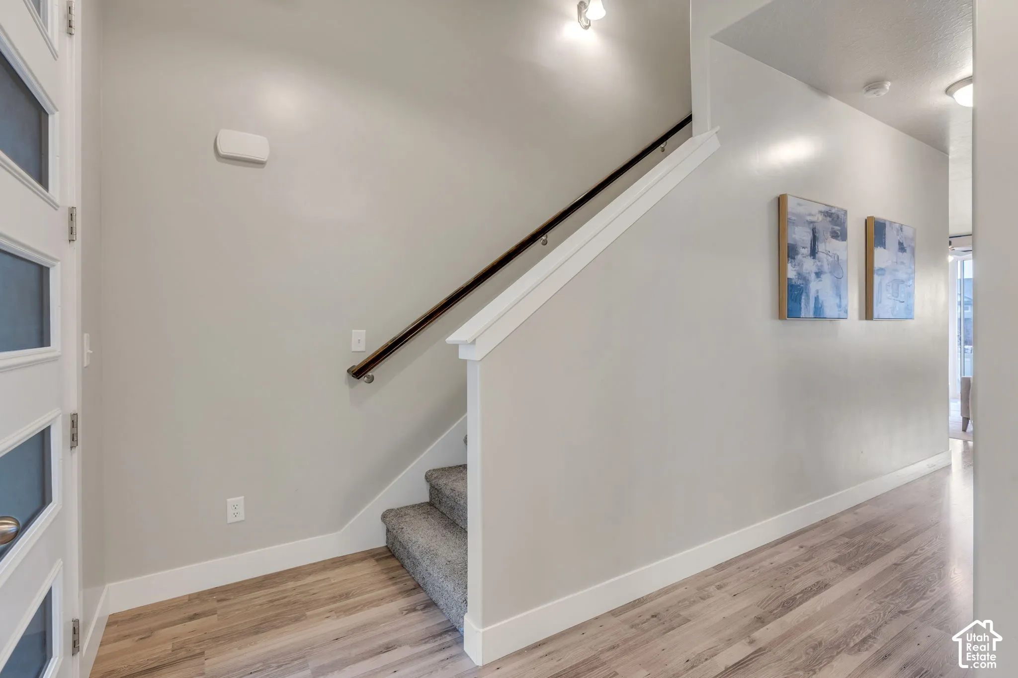 Wood-finish flooring, staircase with carpeted treads and dark wood handrail, white trim, and recessed lighting