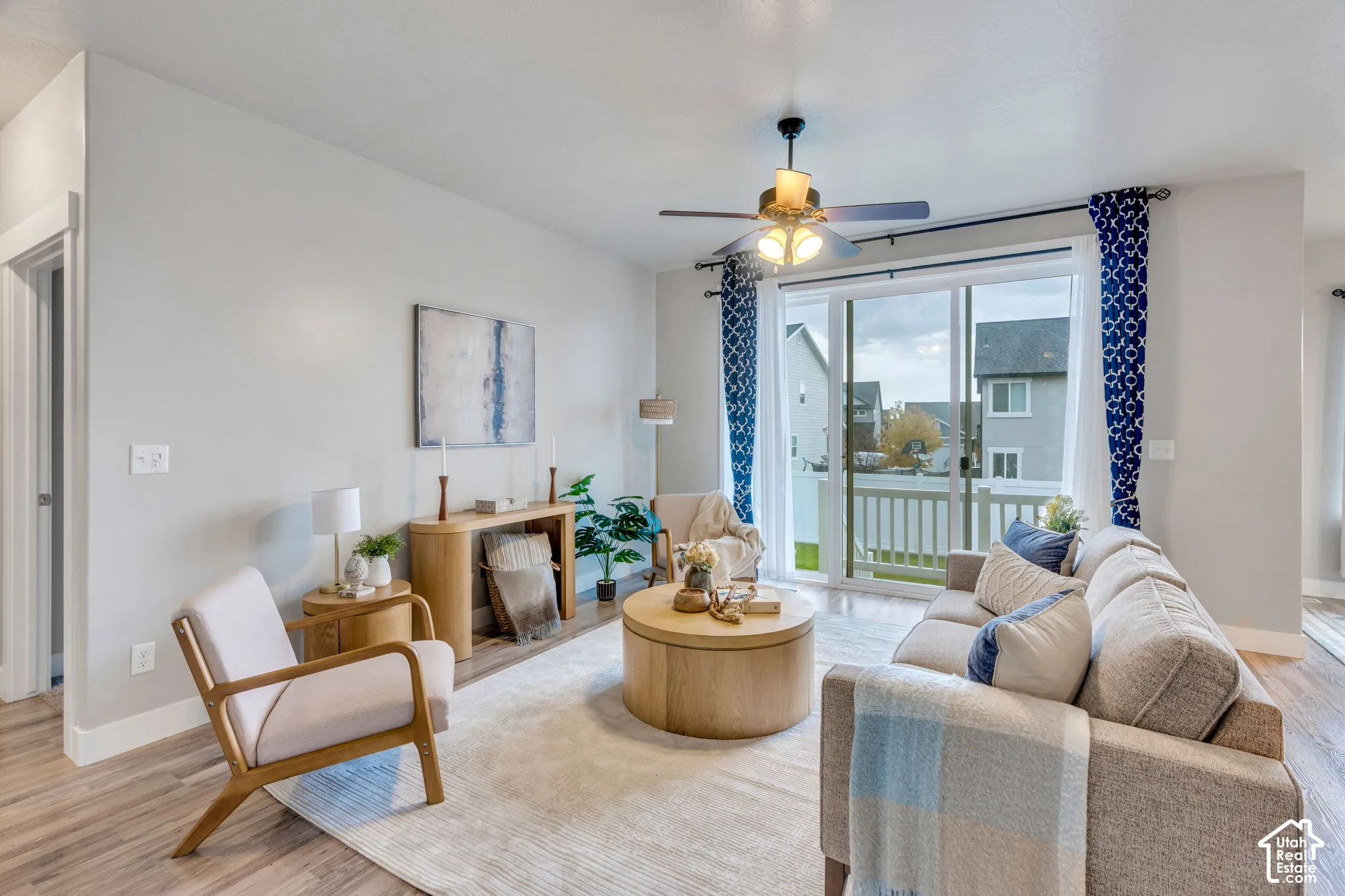 Spacious living area featuring wood-finish flooring, a ceiling fan with integrated lighting, and a sliding glass door leading to an outdoor deck with white railing