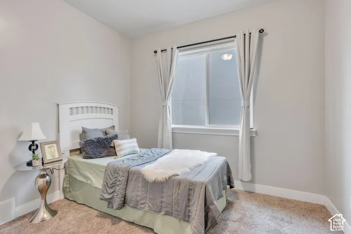 Neutral-toned walls, plush carpet flooring, a white window frame, and a white wood headboard