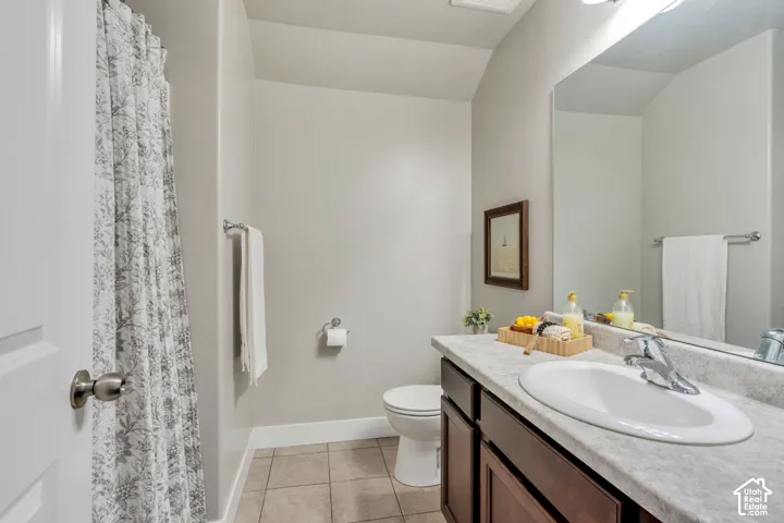 Tiled flooring, vanity with dark wood-finish cabinetry, integrated sink, and an expansive mirror