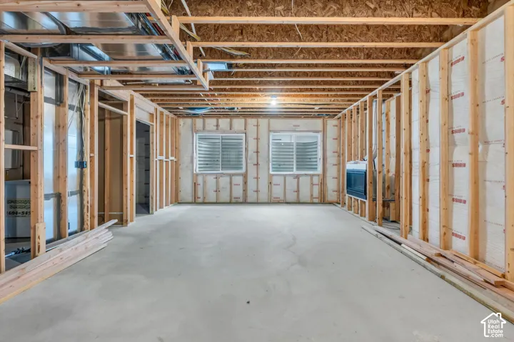 Unfinished space with framed walls, exposed ceiling joists, two visible windows, and concrete flooring