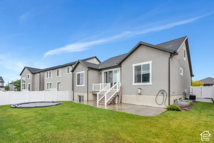Expansive green lawn, white vinyl fencing, concrete patio, and a deck with white railings