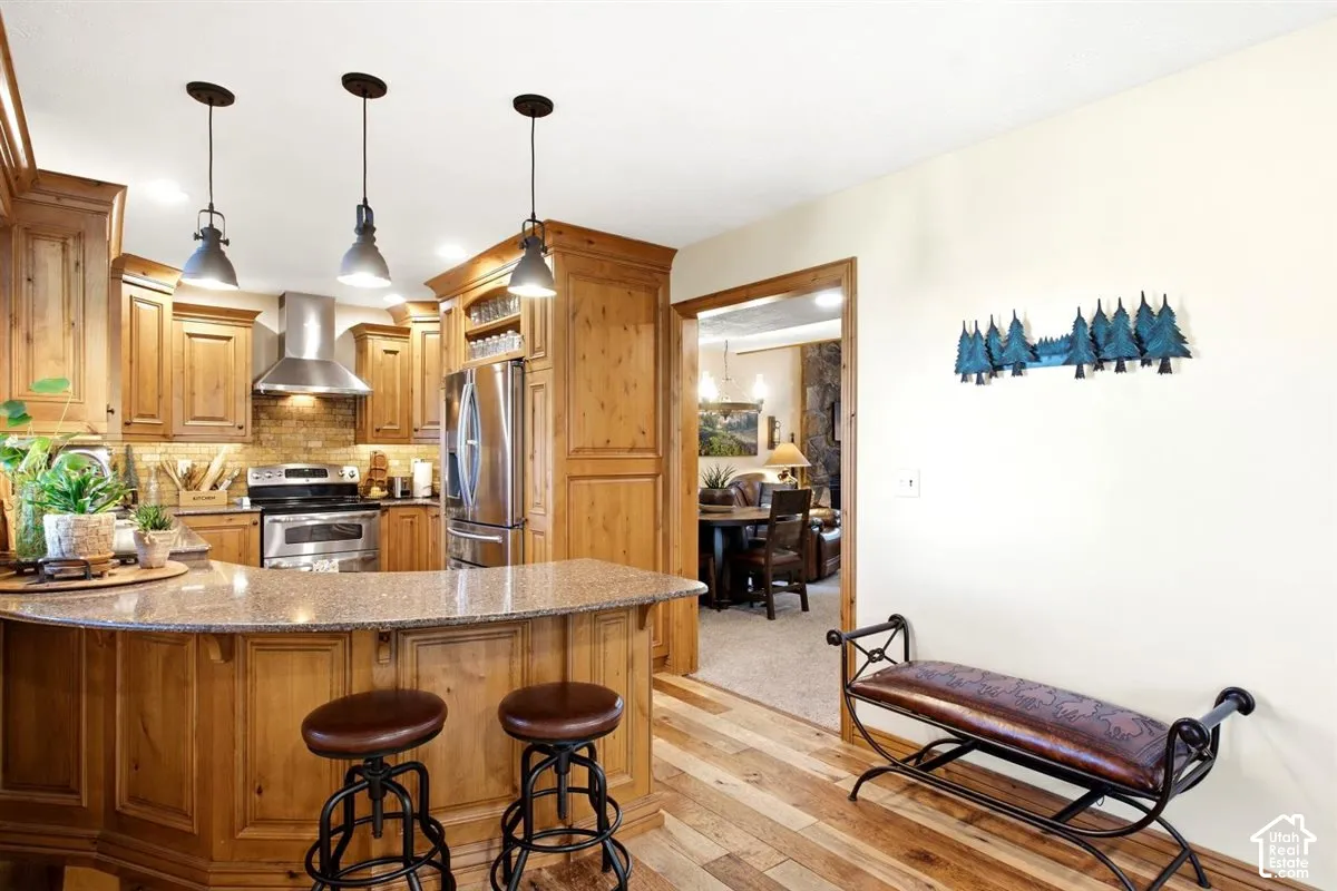 Kitchen featuring wood-finish cabinetry, stainless steel appliances, a tile backsplash, and pendant lighting