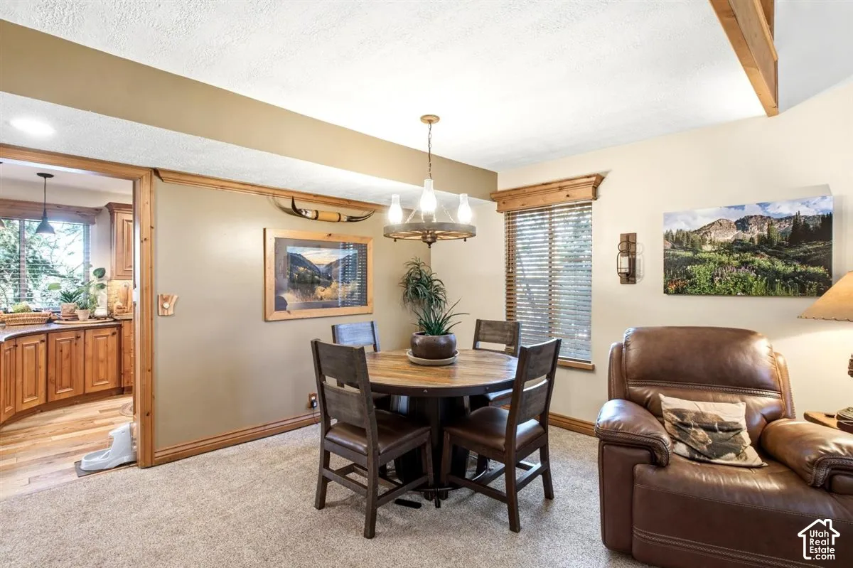 Carpeted floor with a wooden dining table and chairs, wood-finish trim, and a rustic chandelier