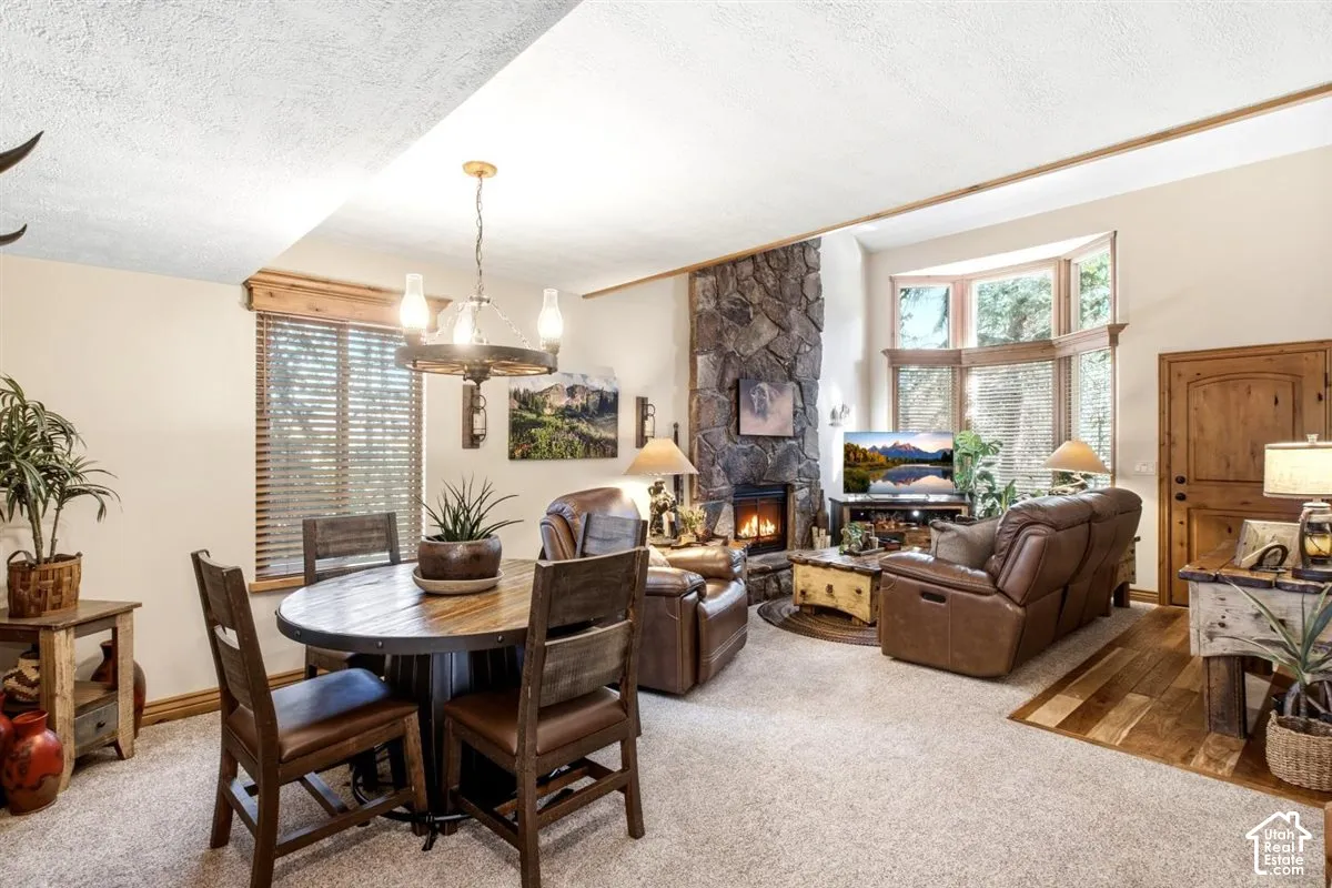 Spacious living area featuring a stone-clad fireplace, bay window, wood-finish flooring, and a circular dining table with a wagon wheel chandelier