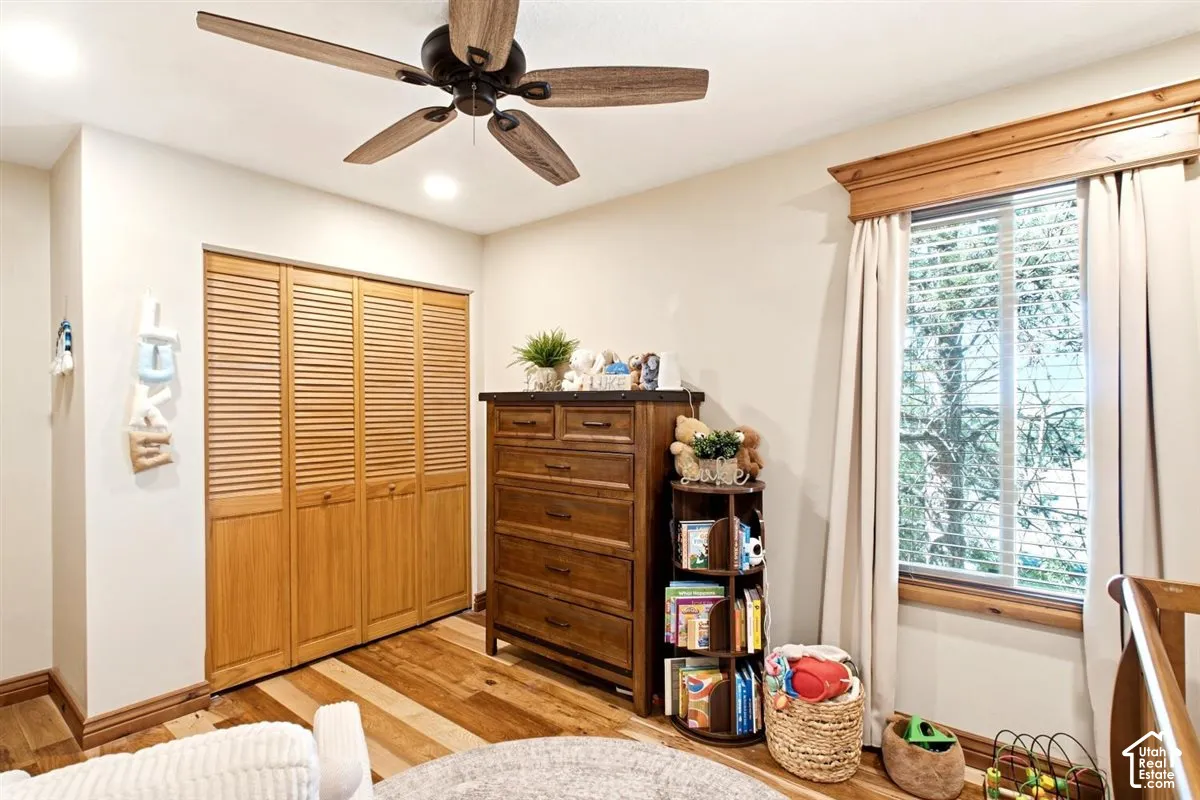 Wood-finish flooring, louvered closet doors, a ceiling fan, a window with blinds, and recessed lighting