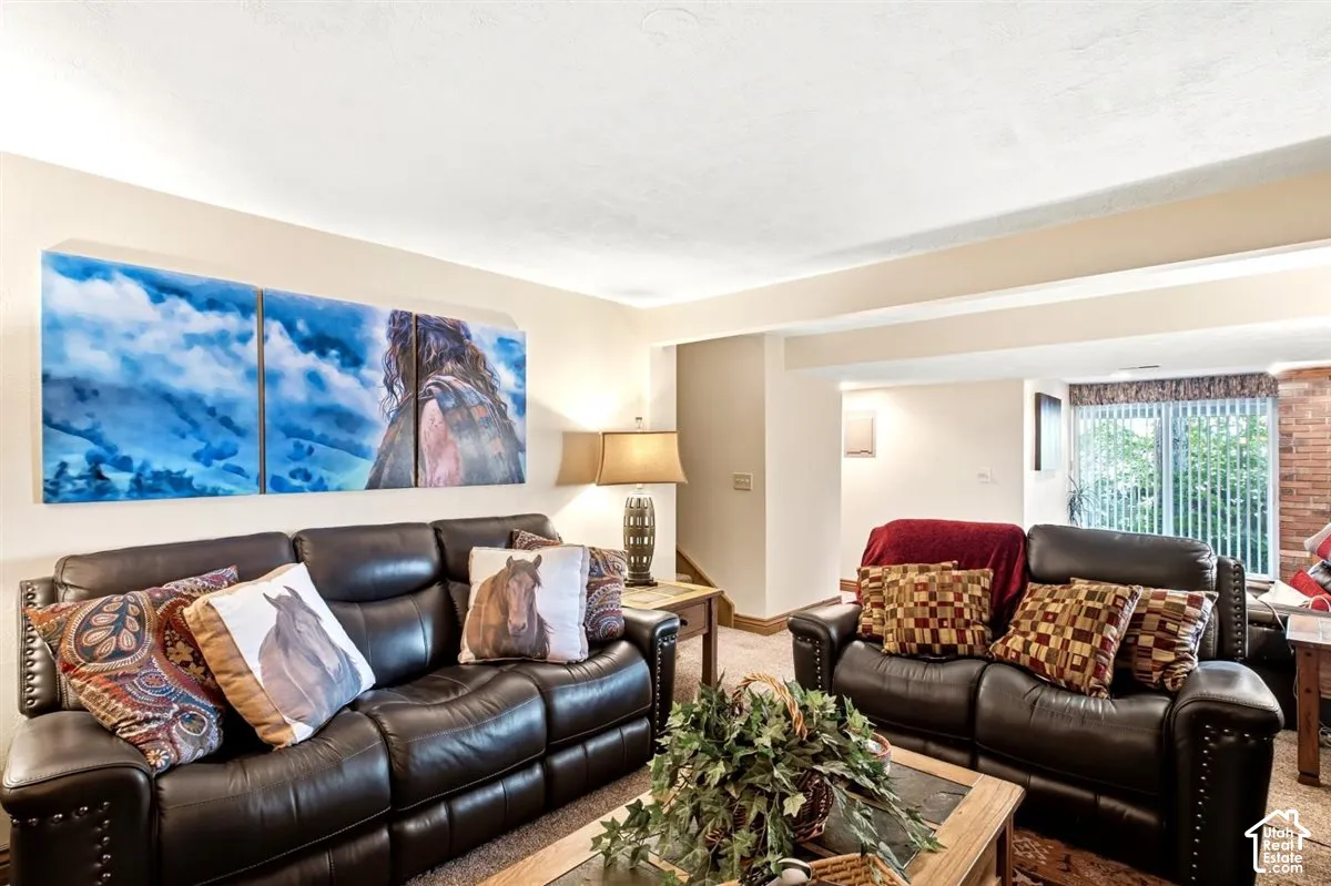 Carpeted living area featuring a neutral wall color, recessed beam ceiling, and a window with vertical blinds