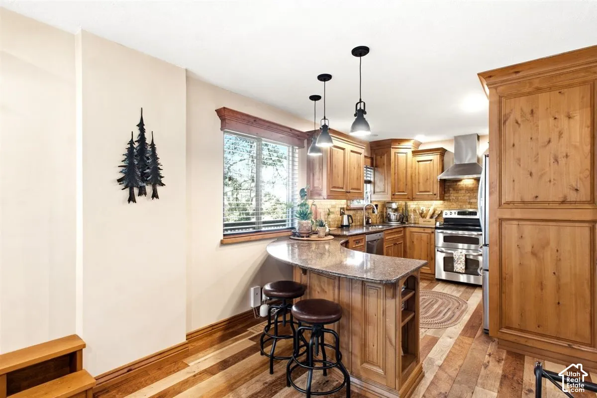 Kitchen featuring wood-finish flooring, natural wood cabinetry, curved island with a stone countertop, and stainless steel appliances