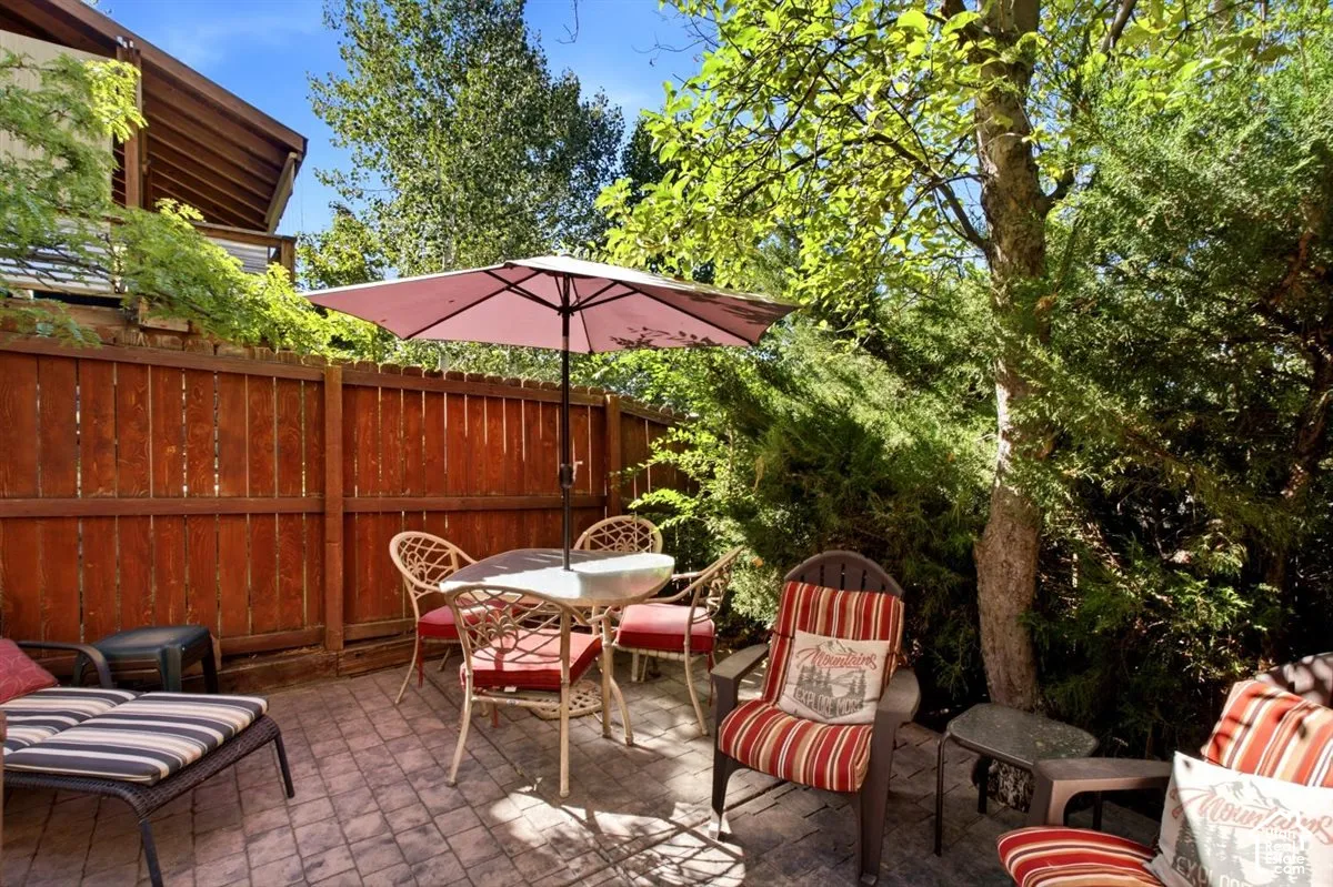 Paved patio area featuring a privacy fence, mature trees, and lush landscaping