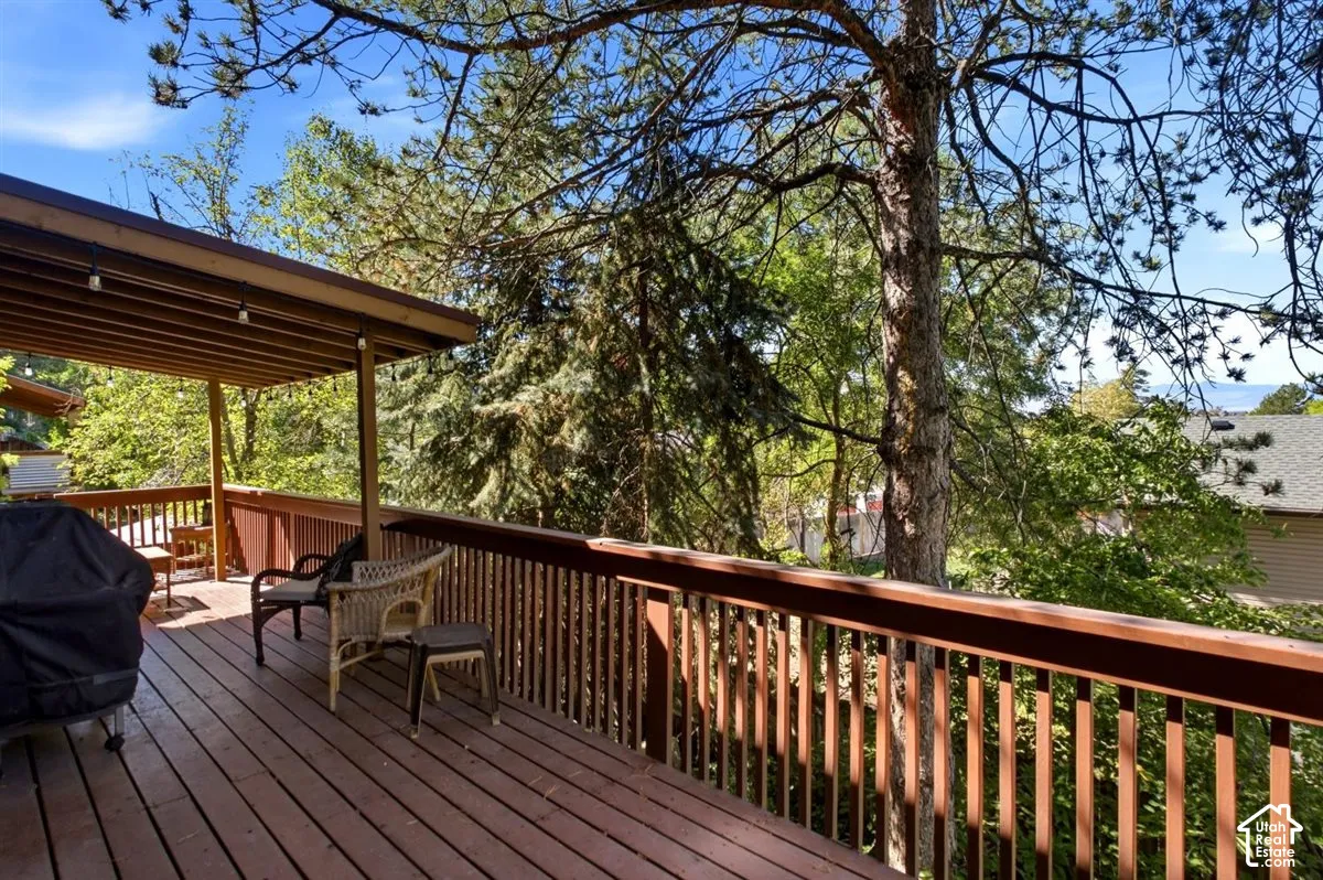 Expansive wood-finish deck with a covered outdoor area, slatted railings, and mature trees providing natural screening