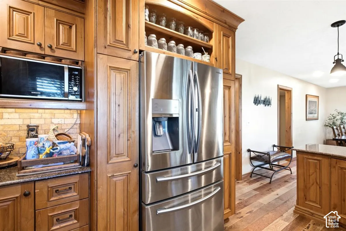 Stainless steel refrigerator, integrated microwave, wood cabinetry, stone-finish backsplash, and wood-finish flooring