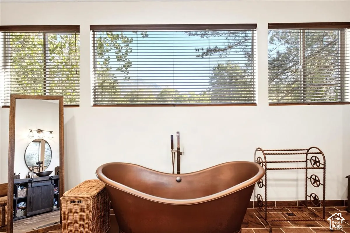 Freestanding copper-finish soaking tub with floor-mounted faucet, wood-finish flooring, and white walls