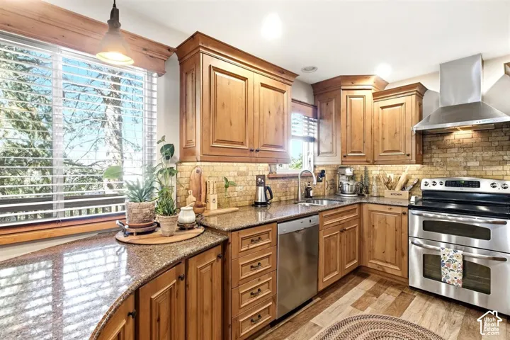 Expansive kitchen featuring a double oven range, stainless steel appliances, wood-finish flooring, ample cabinetry, and a stone tile backsplash