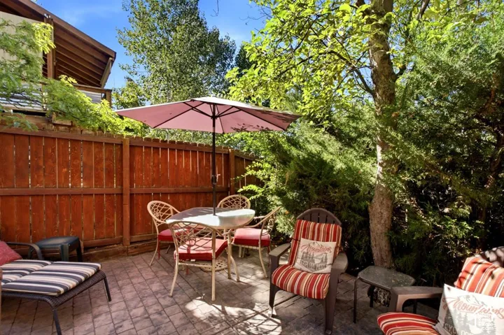 Paved patio area featuring a privacy fence, mature trees, and lush landscaping