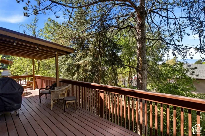 Expansive wood-finish deck with a covered outdoor area, slatted railings, and mature trees providing natural screening