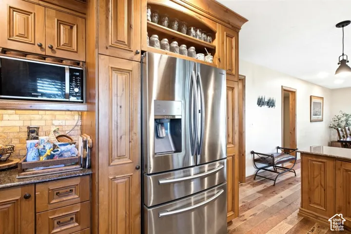 Stainless steel refrigerator, integrated microwave, wood cabinetry, stone-finish backsplash, and wood-finish flooring