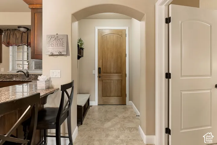 Archway entry featuring a light wood-finish door, tiled flooring, and a kitchen counter with a stone-finish surface