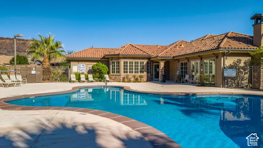 Resort-style pool with a concrete deck, surrounded by a building with a tile roof and stucco exterior