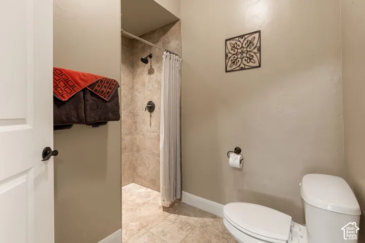 Tiled shower with dark bronze fixtures, tile flooring, and a white toilet