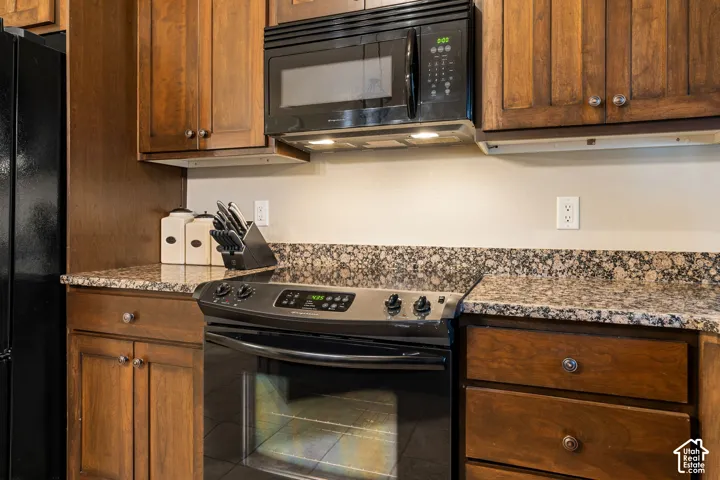 Rich wood cabinetry with circular pulls, patterned stone countertops, stainless steel and black oven, and an overhead microwave