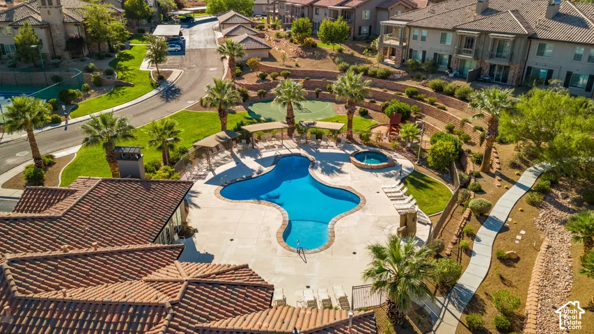 Resort-style pool with integrated spa, adjacent tennis court, mature palm trees, terraced landscaping, and paved walking path