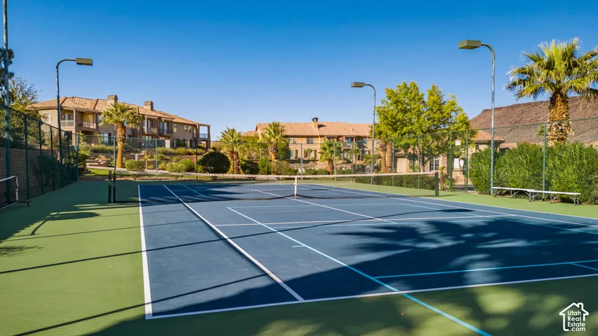 Tennis court with blue playing surface and green surrounds, featuring perimeter fencing and court lighting