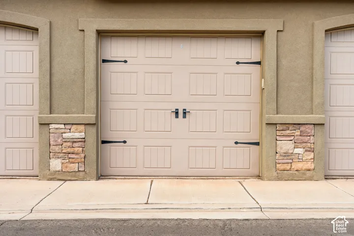 Stucco exterior with stone accents, featuring a panel-style garage door with decorative hardware