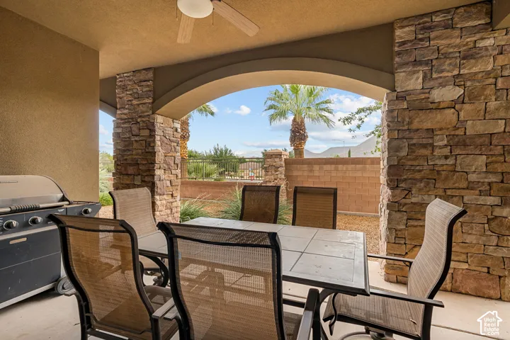 Covered patio featuring a ceiling fan, stone-clad architectural columns, arched openings, and a paved surface